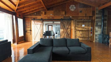 A rustic interior with a large sectional sofa, wooden walls, a clock, and a fireplace.