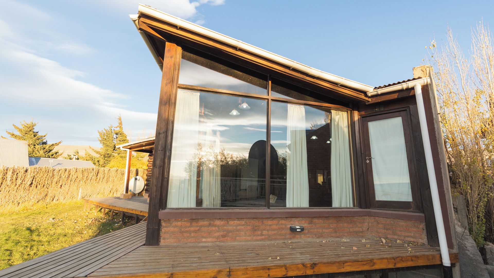 A modern house with a large glass window, a wooden deck, and a brick foundation.