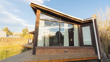 A modern house with a large glass window, a wooden deck, and a brick foundation.