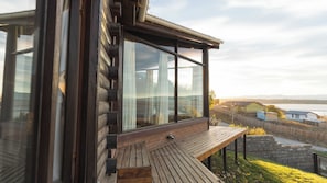 A modern log cabin with large windows, a wooden deck, and a view of a lake and distant houses. - Hermosa y amplia casa con vista al lago (El Calafate)