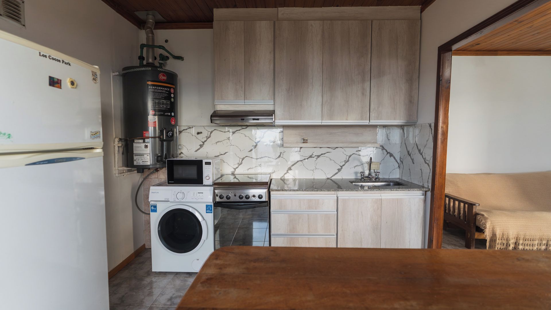 Una cocina compacta equipada con lavadora, microondas, estufa y calentador de agua.