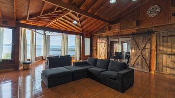 Un salón amplio con un sofá seccional grande, vigas de madera en el techo y vistas al mar.