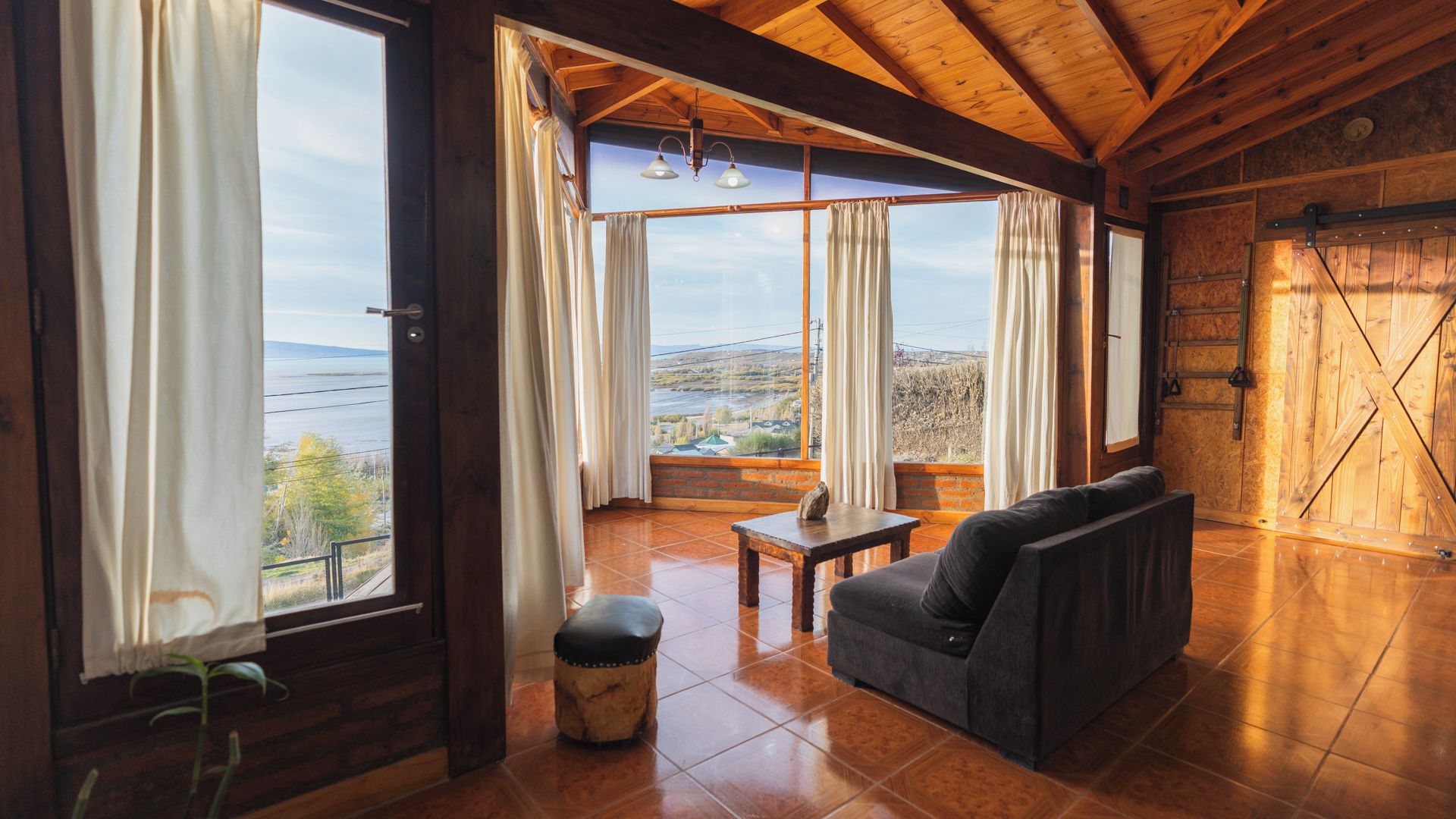 Un intérieur rustique avec un canapé, une petite table et une vue sur une rivière et le paysage, grâce à de grandes fenêtres.