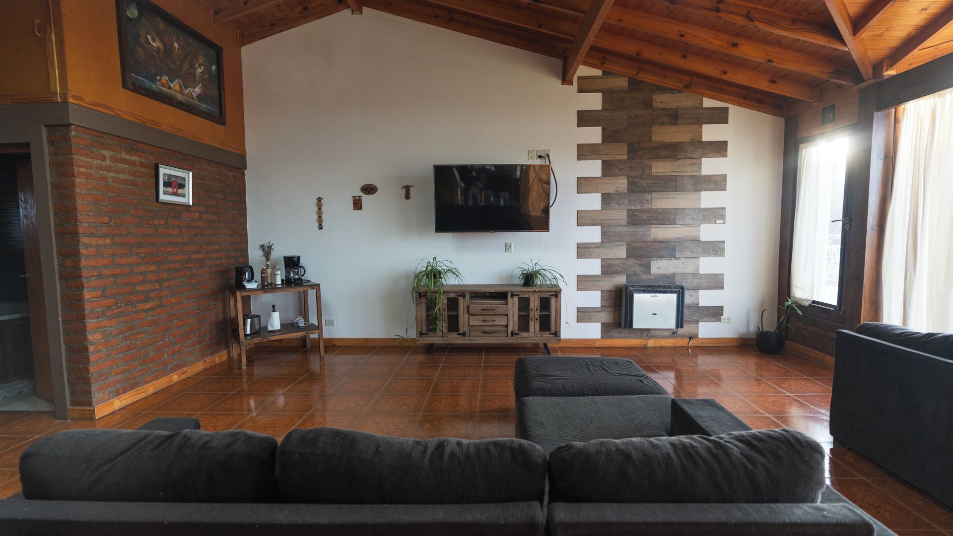 A living room with a wooden ceiling, a flat-screen TV, a brick wall, a wooden cabinet, and a sofa.