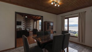 Amplia sala de estar con mesa de comedor, sillas y vista a una masa de agua a través de grandes ventanales.