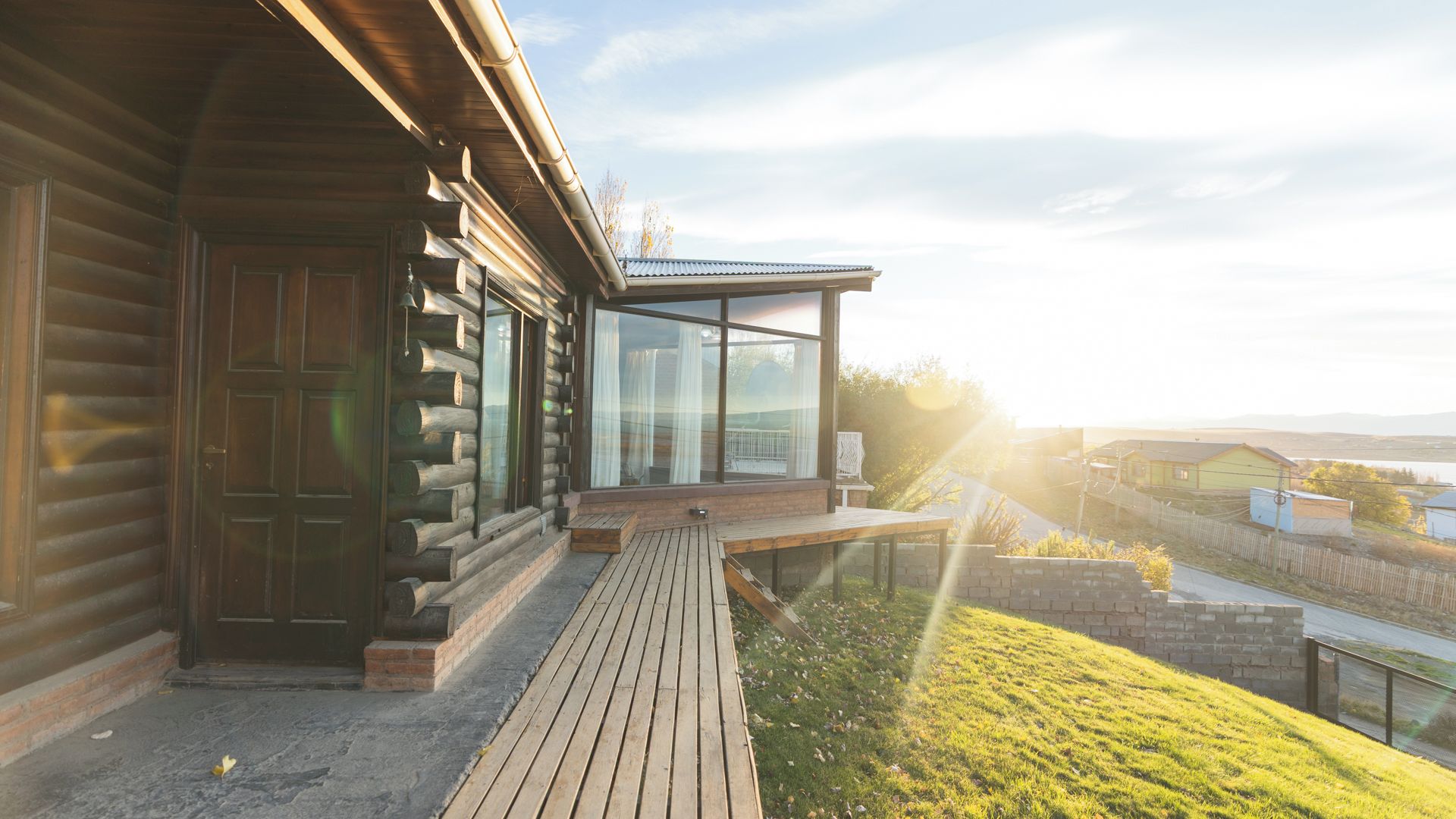 A log cabin with a deck and a glass enclosure overlooking a landscape.