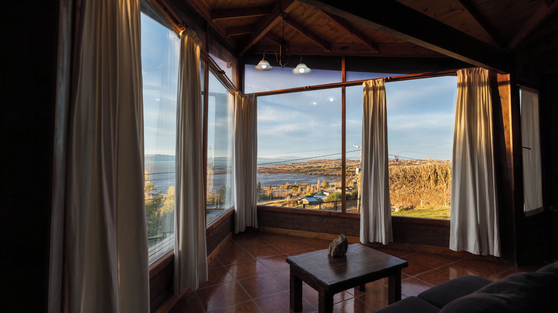 A room with large windows, a wooden ceiling, and a stone table.