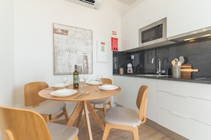 A modern kitchen with white cabinets, a black countertop, and stainless steel appliances. There is a dining table set with plates, glasses, and cutlery. - Proteia Studio by Atlantic Holiday (Santa Cruz)