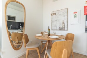 A dining area with a round table, four chairs, a wine bottle, and a large mirror. - Proteia Studio by Atlantic Holiday (Santa Cruz)