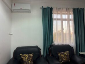 A room with two black leather chairs, a window with green curtains, and an air conditioning unit on the wall. - Delightful 2-bedrooms apartment with AC in Dar es Salaam (Dar es Salaam)