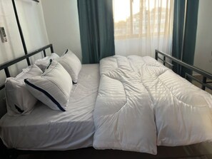 A bed with white bedding and pillows, a window with curtains, and a metal headboard. - Delightful 2-bedrooms apartment with AC in Dar es Salaam (Dar es Salaam)
