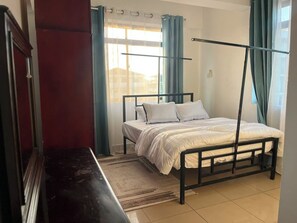 A bedroom with a bed, curtains, a window, and a radiator. - Delightful 2-bedrooms apartment with AC in Dar es Salaam (Dar es Salaam)