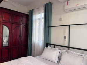 Ein Hotelzimmer mit einem Bett, einem Kleiderschrank, einem Fenster mit Vorhängen und einer Klimaanlage.