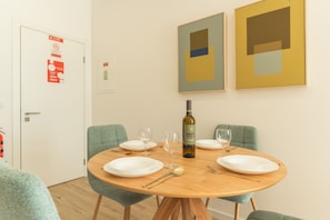 A dining area with a round table, four chairs, and a bottle of wine. There are two framed abstract paintings on the wall. - Rosa Studio by Atlantic Holiday (Santa Cruz)