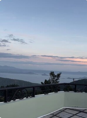 A balcony with a view of a body of water and distant mountains. - Casa Alegre Spacious Home - Rooftop Tall View, Near Tourist Spots and Malls (Tagaytay City)