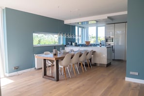 A modern kitchen with a dining area, large windows, and a view of greenery outside. - Villa Topduin, with a sauna, close to the sea (Bergen aan zee)