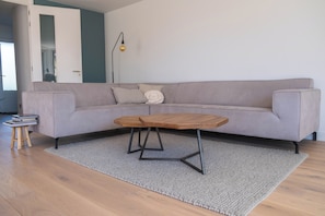A living room with a grey sofa, a wooden coffee table, and a small wooden stool with books. - Villa Topduin, with a sauna, close to the sea (Bergen aan zee)
