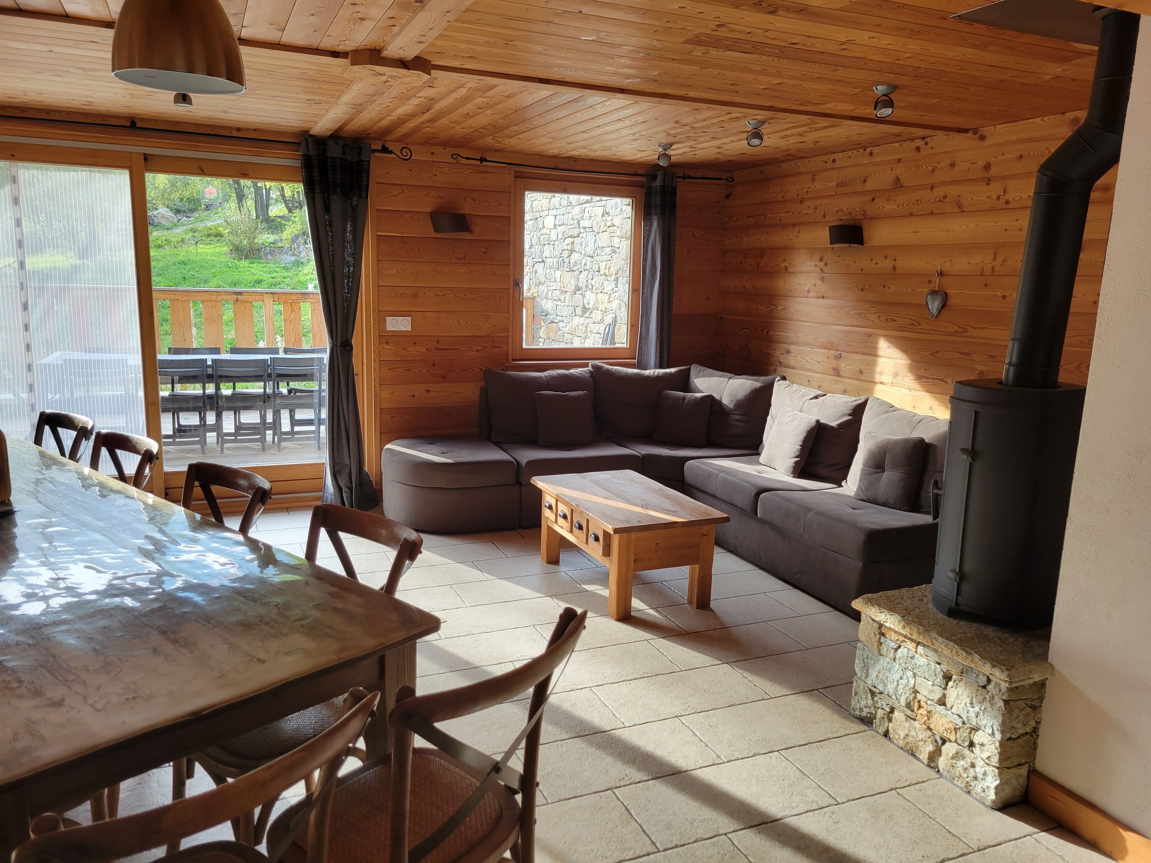 Gemütliches Blockhaus-Interieur mit Holztisch, gepolsterten Sitzgelegenheiten, einem Kamin aus Stein und Blick ins Freie.