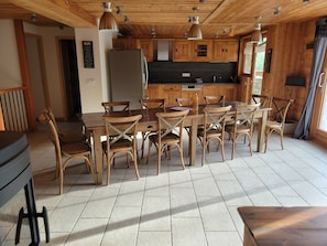 En inredning med träpanel, ett matbord omgivet av stolar, ett kylskåp och ett köksområde med skåp och en bänkskiva.
