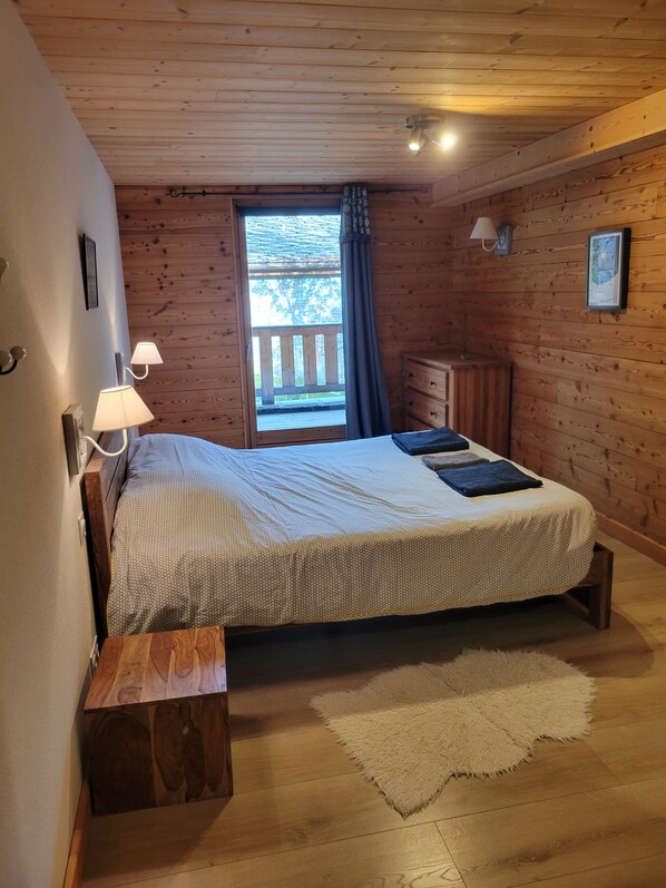 A wooden cabin bedroom with a bed, bedside lamps, a dresser, and a window with curtains.
