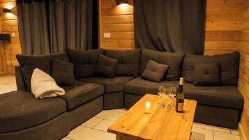 Eine gemütliche Ecke mit einem dunkelgrauen Ecksofa, einem Holztisch und einer Weinflasche.