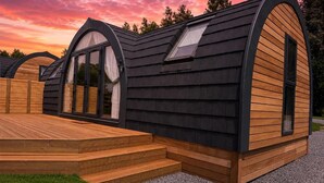 Una cabaña moderna de un piso con techo inclinado, ventanas amplias y una terraza de madera.