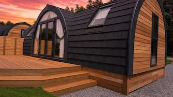 Una cabaña moderna de un piso con techo inclinado, ventanas amplias y una terraza de madera.