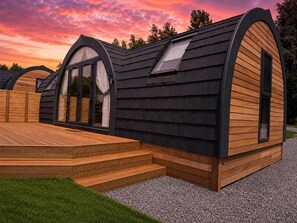 Una cabaña moderna de un piso con techo inclinado, ventanas amplias y una terraza de madera.