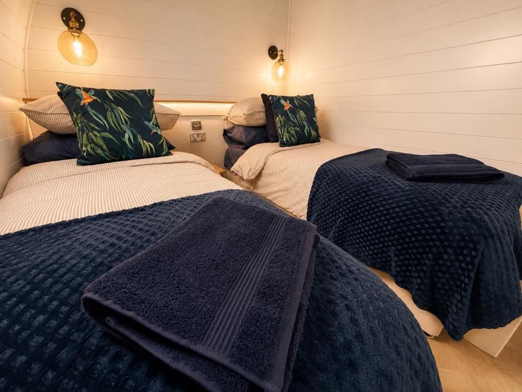 Quarto de hotel com duas camas, cada uma com um cobertor azul escuro e uma almofada estampada com folhagens tropicais.