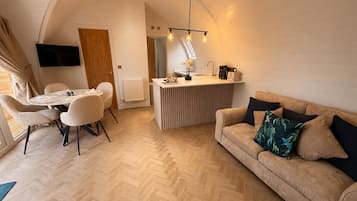 Um interior moderno com área de refeições, cozinha compacta, sofá e TV fixada na parede.