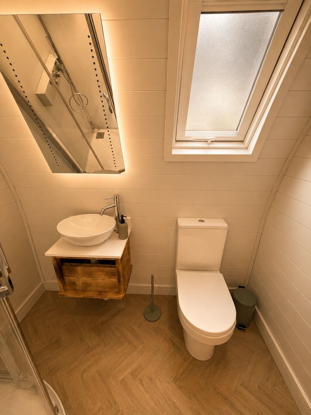 A compact bathroom with a white sink, toilet, and a skylight above.