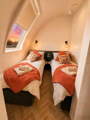 Una habitación pequeña y acogedora con dos camas, un tragaluz y vistas al atardecer.