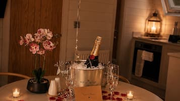 A round table with a bottle of champagne, glasses, a candle, and rose petals.