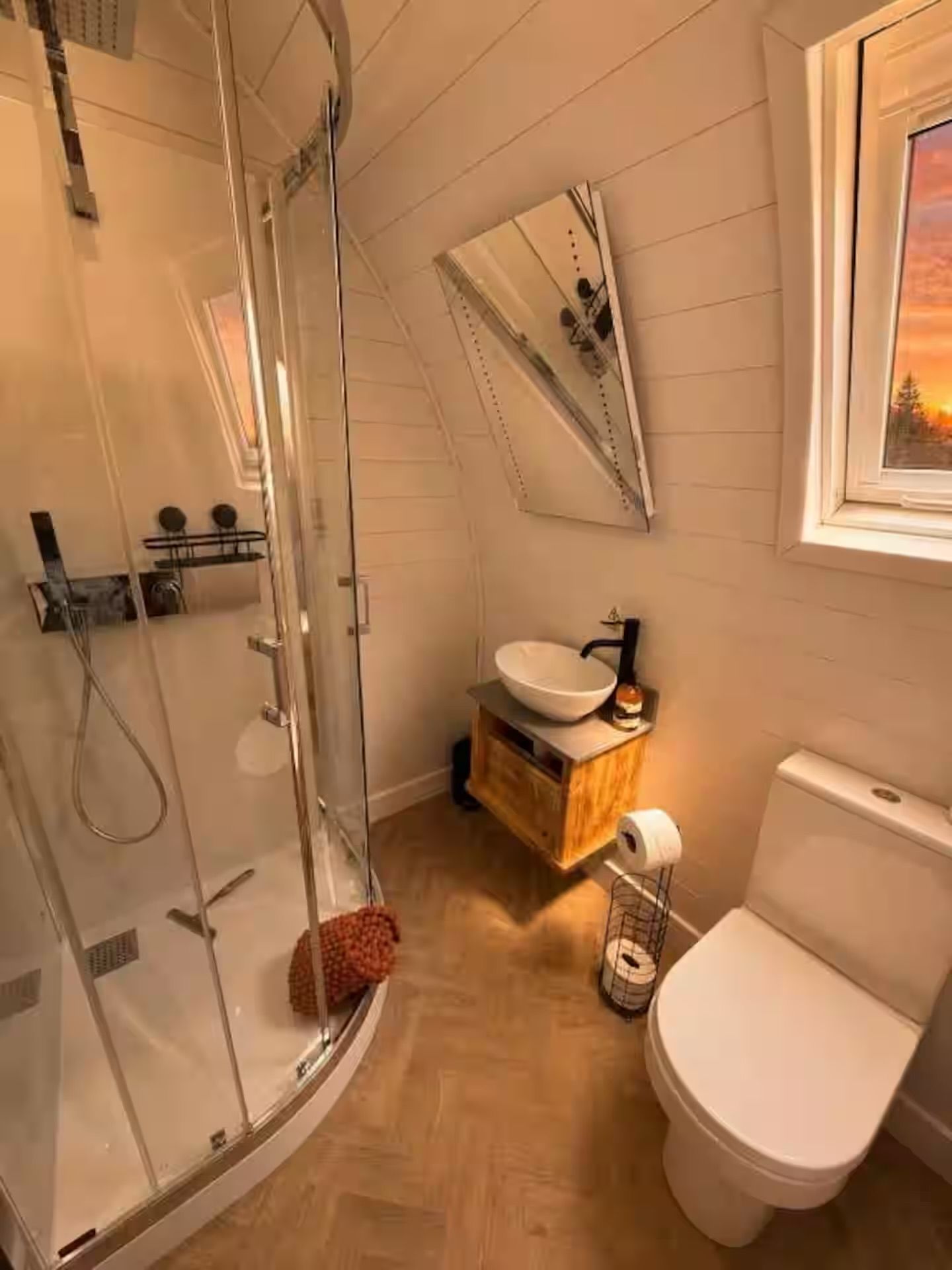 Un baño con cabina de ducha de vidrio, un lavabo blanco con tocador de madera y un inodoro blanco.