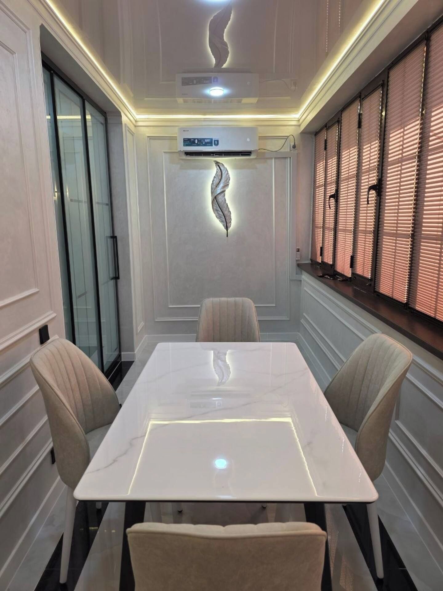 A conference room with a marble table, cushioned chairs, a decorative wall piece, and a window with blinds.