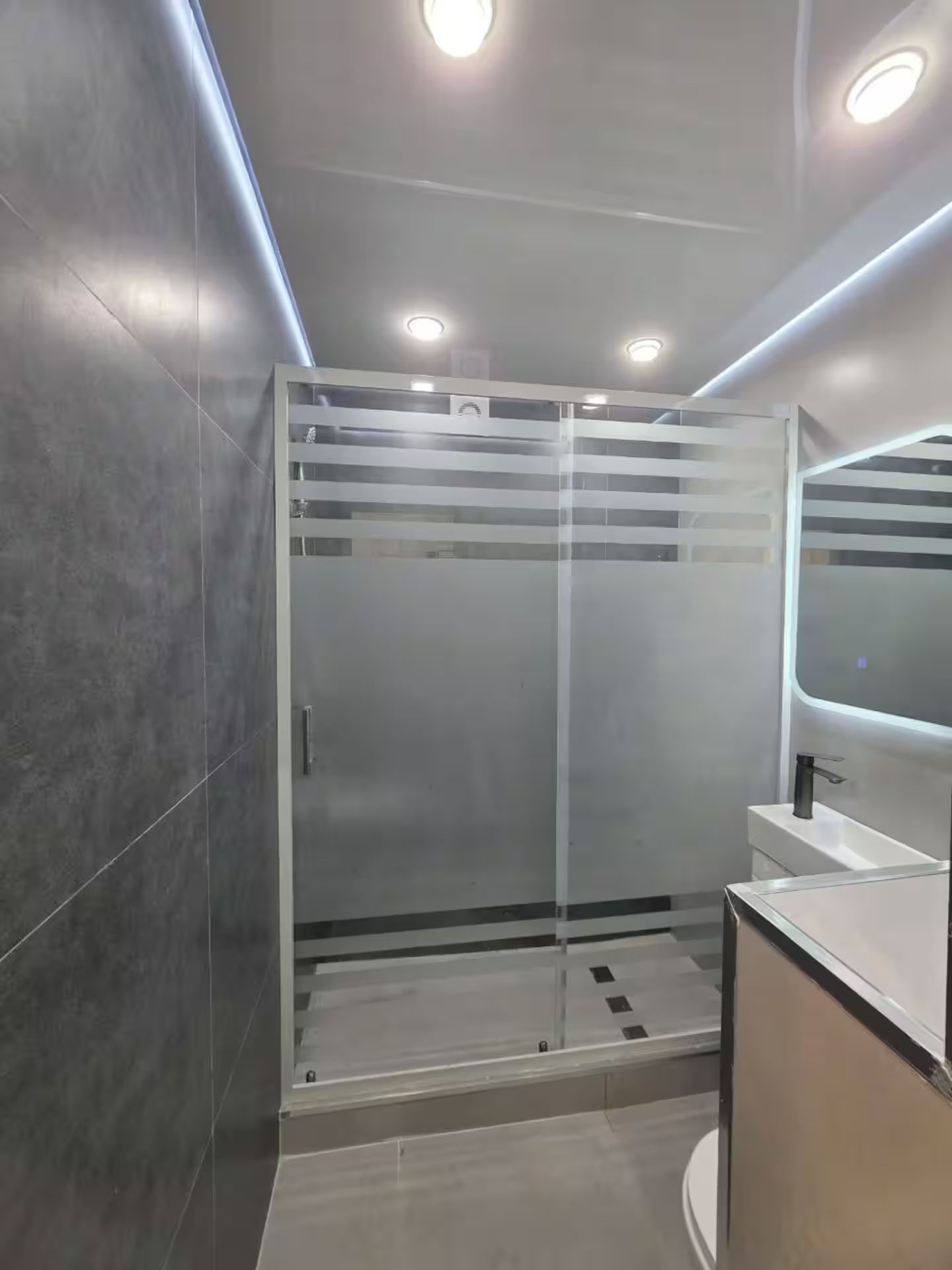 Un baño moderno con cabina de ducha de vidrio, lavamanos con espejo e iluminación empotrada en el techo.