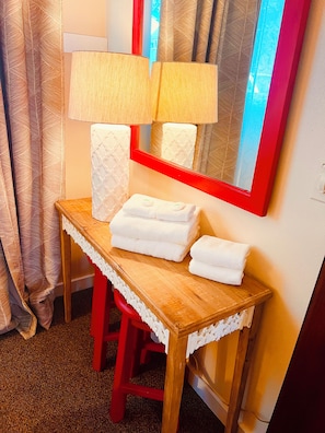 Una mesa de madera con un espejo, dos lámparas y una pila de toallas blancas.