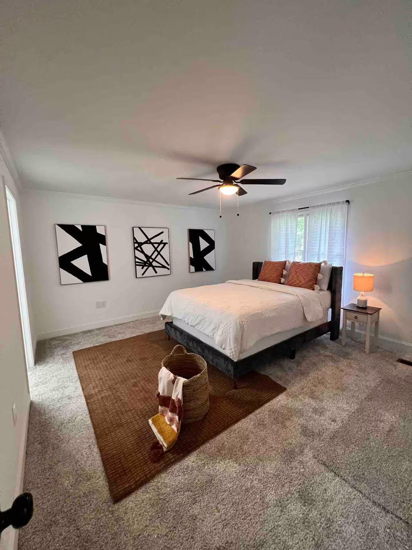 Une chambre à coucher avec un lit, un ventilateur de plafond, un tapis et des œuvres d’art abstraites accrochées au mur.