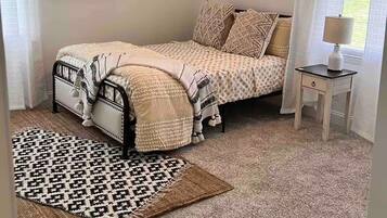 A bedroom with a bed, a ceiling fan, a nightstand, a lamp, a rug, and a window with curtains.