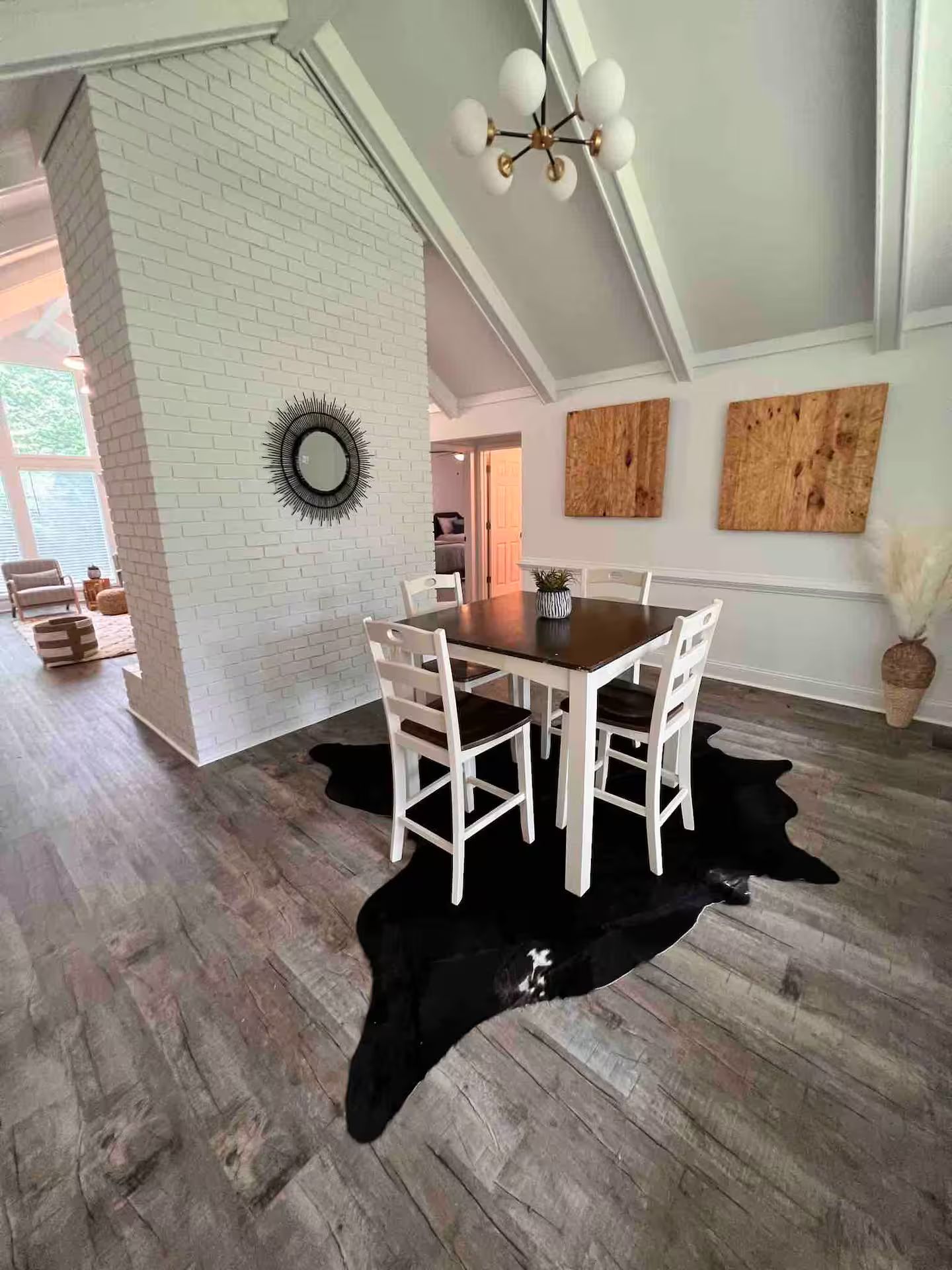 A dining area with a wooden table and chairs, a black cowhide rug, and a white brick wall.
