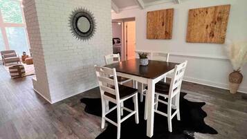 A dining area with a wooden table and chairs, a black cowhide rug, and a white brick wall.