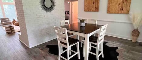 A dining area with a wooden table and chairs, a black cowhide rug, and a white brick wall.