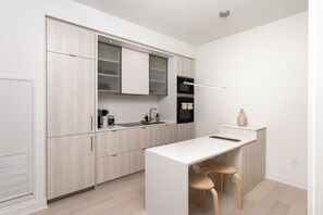 Une cuisine moderne avec des meubles de couleur bois clair, un plan de travail blanc et un four encastré.