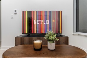 Un salon moderne avec un téléviseur à écran plat fixé sur un meuble en bois, un porte-bougie en verre et une plante en pot sur une table en bois.