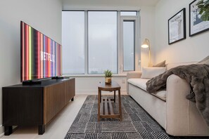 Un salon moderne doté d’un grand téléviseur à écran plat, d’un canapé, d’une table basse et d’une fenêtre offrant une belle vue.