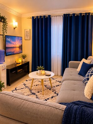 Ein Wohnzimmer mit einer Couch, einem Couchtisch, einem Fernseher und Vorhängen.