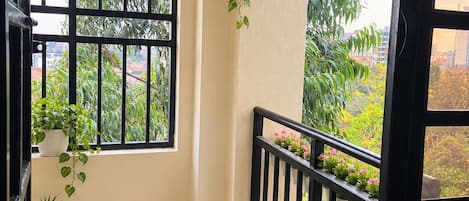 Un balcon donnant sur un espace verdoyant, une plante suspendue, une lanterne et une rambarde.