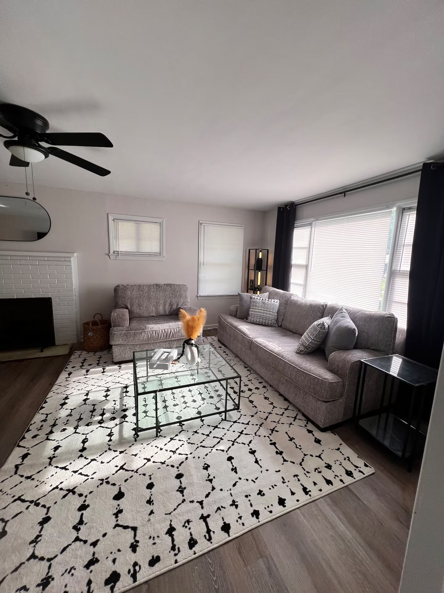 A modern living room with a glass coffee table, grey sofas, a patterned rug, and a fireplace.