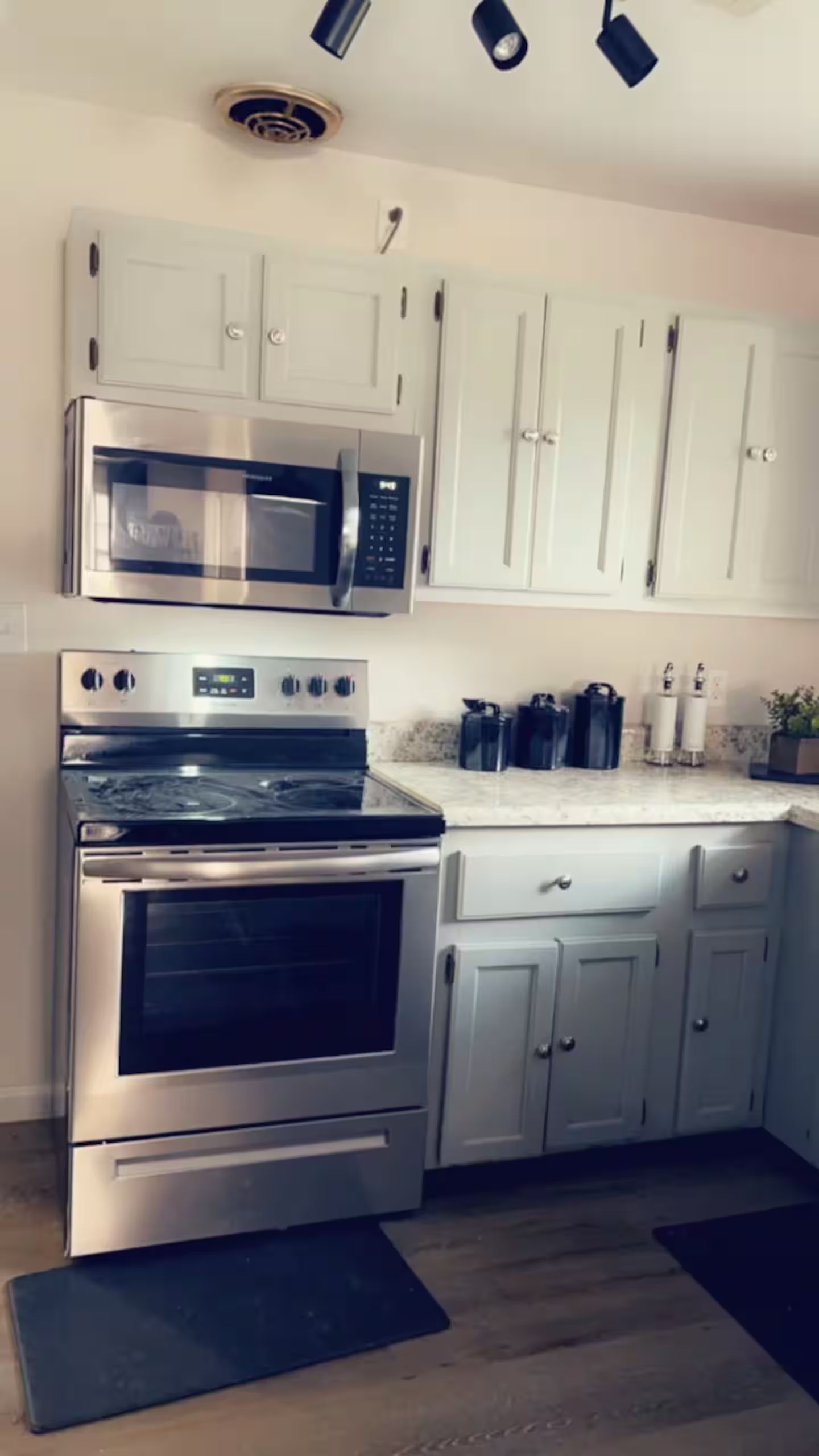 A kitchen with stainless steel appliances, white cabinets, and a black mat on the floor.