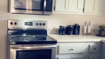 A kitchen with stainless steel appliances, white cabinets, and a black mat on the floor.